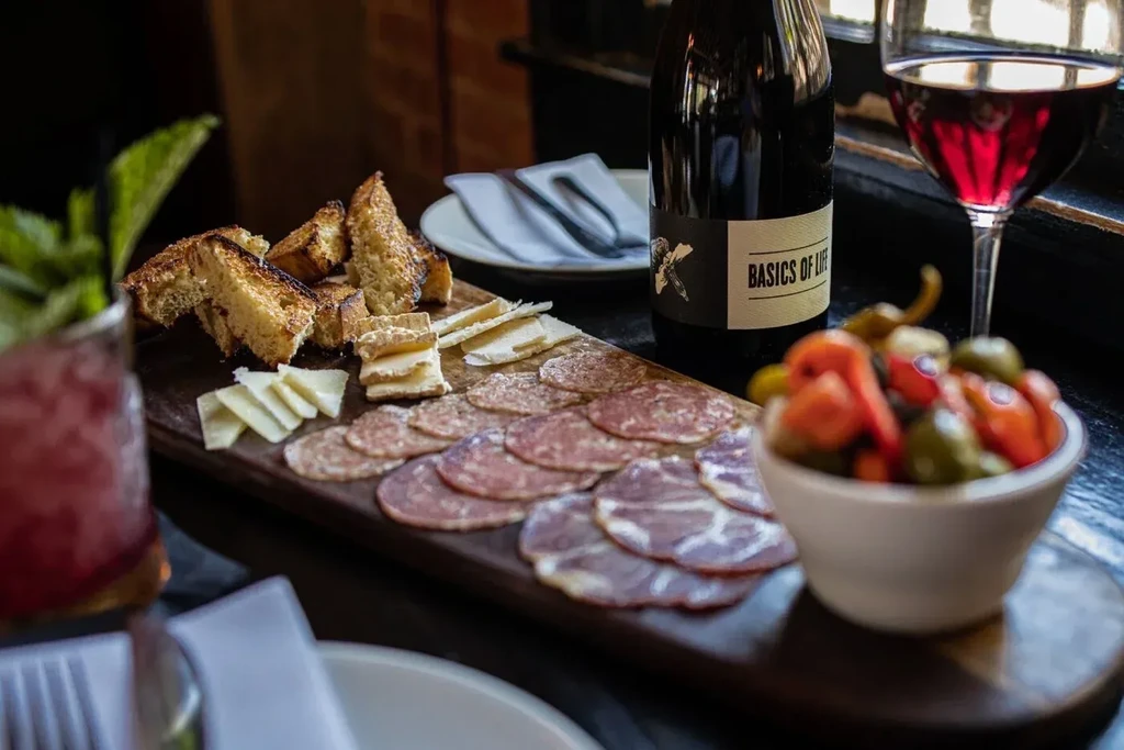 Charcuterie board with meats, cheeses, wine, cocktail, and pickled peppers.