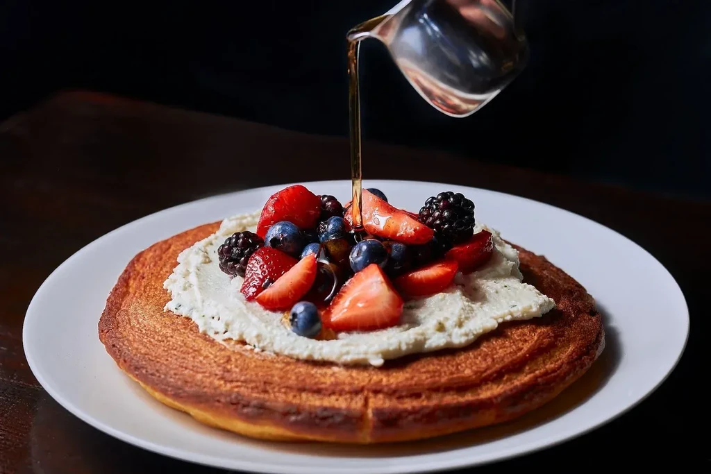 Pancake with whipped cream, fresh berries, and pouring syrup.