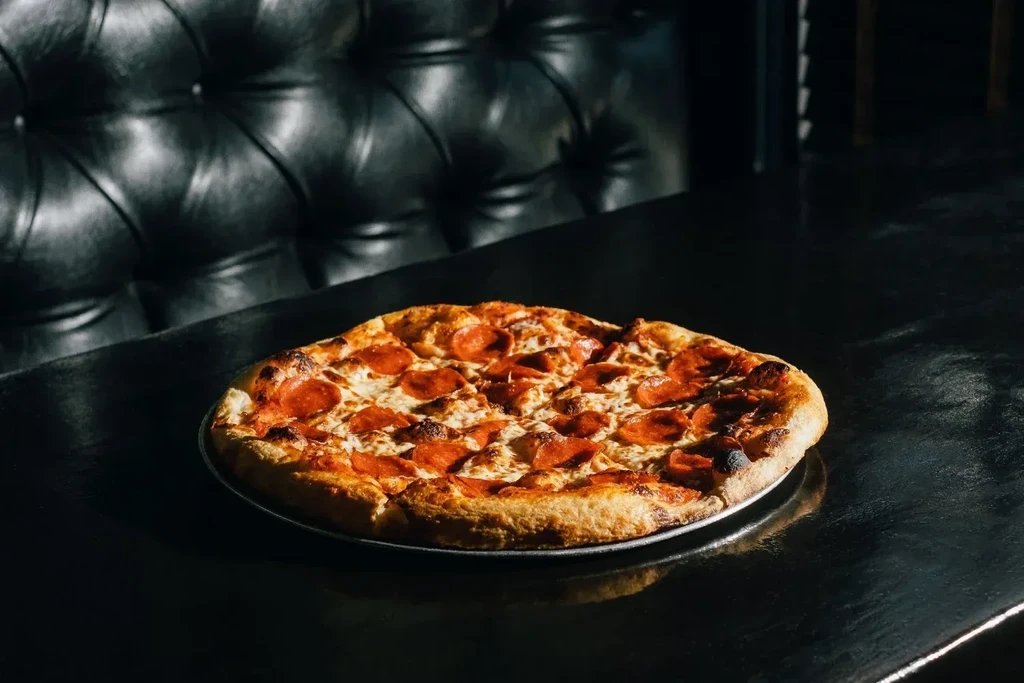 Whole pepperoni pizza on a pan, in a dark restaurant setting.