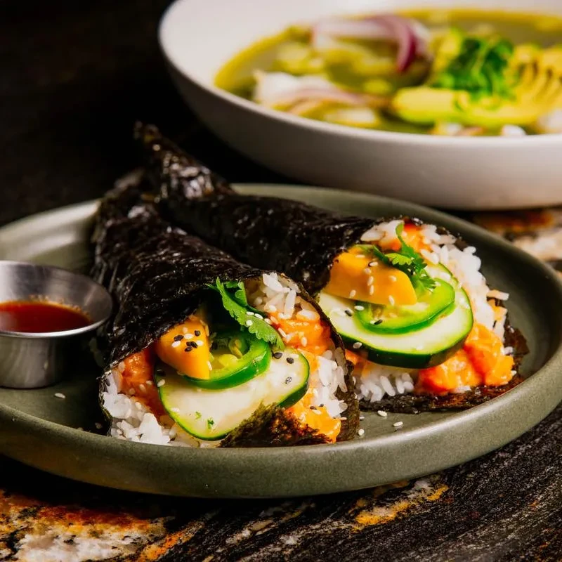 Two elaborate temaki hand rolls with fish, rice, cucumber, and yellow fruit.