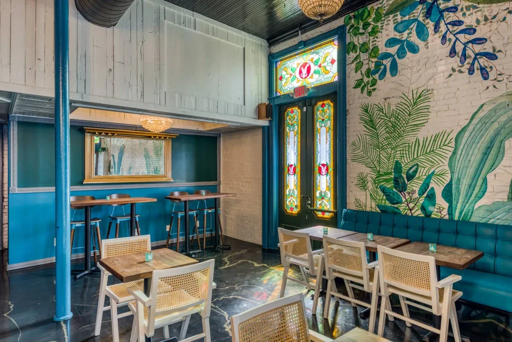Eclectic restaurant interior with teal walls, tropical mural, and decorative stained glass.