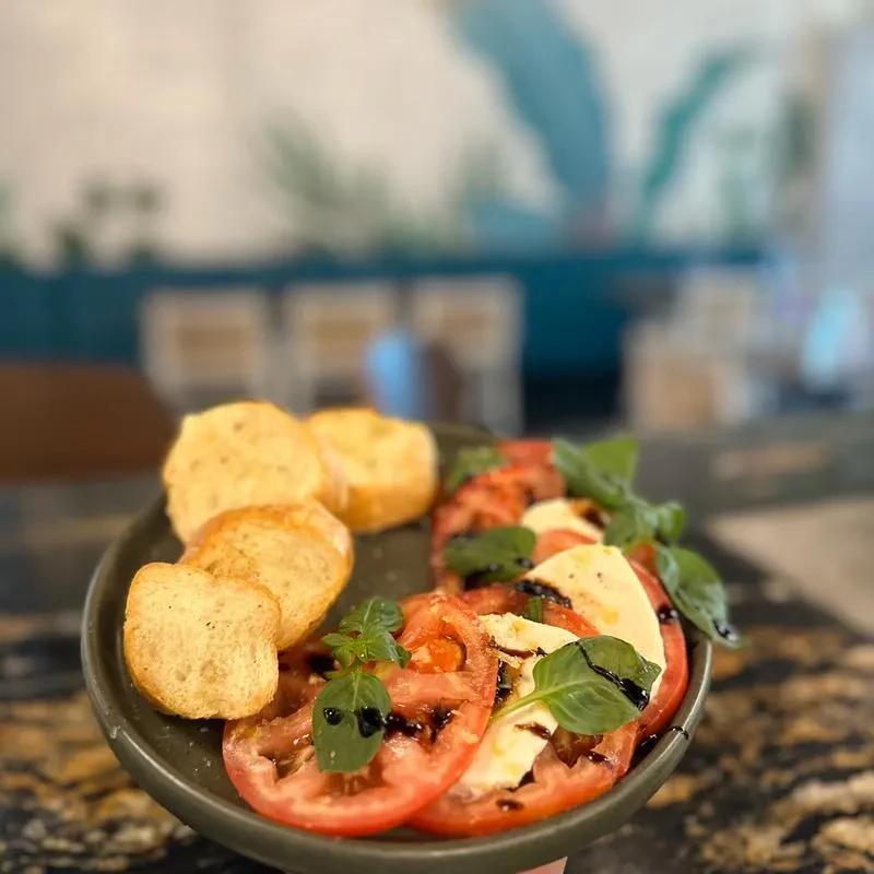 Sliced Caprese salad with balsamic glaze, basil, and toasted crostini.