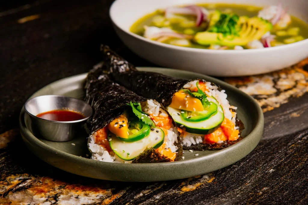 Two temaki hand rolls with salmon, mango, cucumber, and dipping sauce.