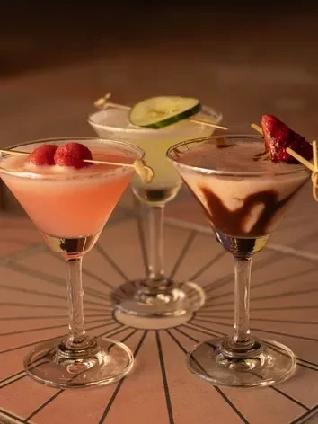 Pink, yellow, and brown cocktails in martini glasses with fruit and cucumber.
