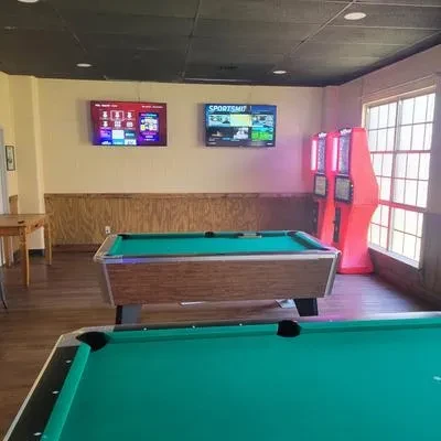 Interior with two green pool tables, TVs, and red arcade machines.