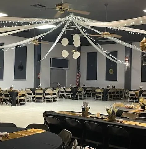 Large, empty event hall with black tables, gold accents, and draped lighting.