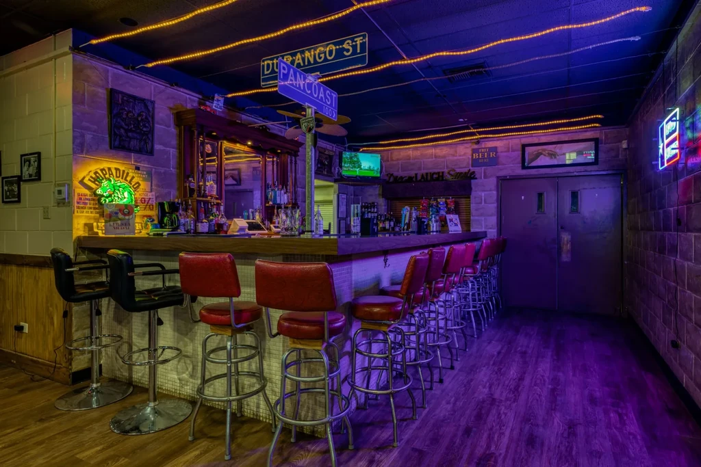 Colorful, empty bar interior featuring a long counter and decorative signs.
