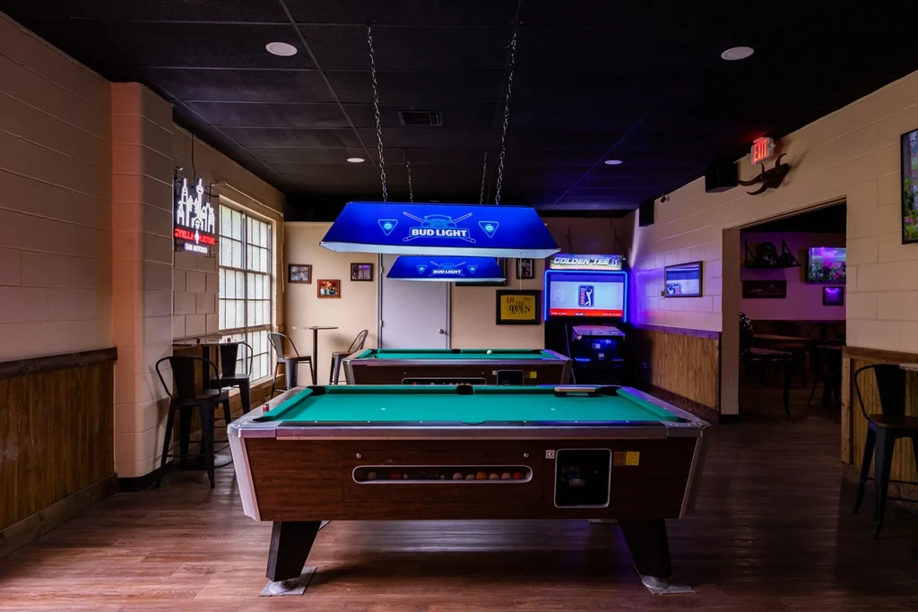 Two green pool tables and arcade game in a bar interior.