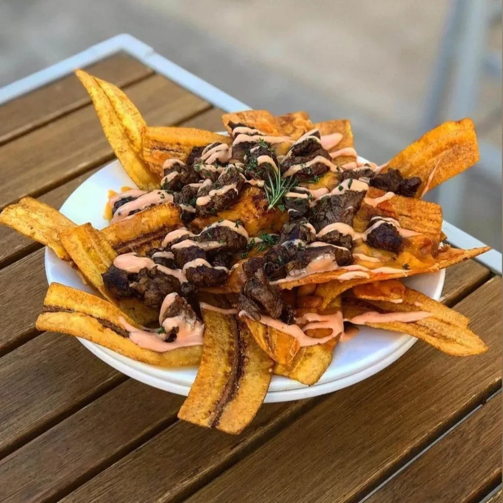 Golden plantain nachos with dark meat, pink sauce, and rosemary garnish.