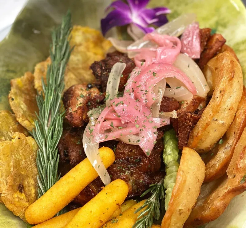 Vibrant fried meat platter with plantains, potatoes, yucca, and garnishes.