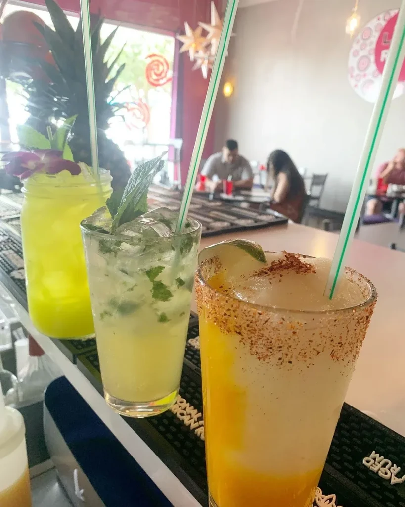 Three colorful, garnished drinks on a bar counter in a restaurant.