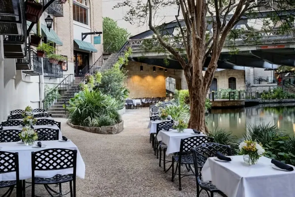 Empty riverside dining area with set tables and a background bridge.