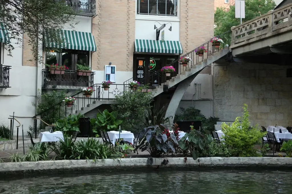 Outdoor dining by water, brick building, awnings, and ornate staircase.