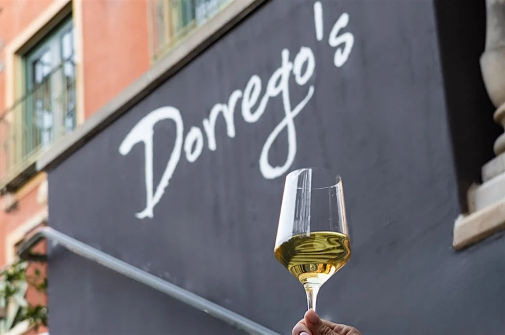 Hand holds white wine glass; Dorrego's restaurant sign and building.