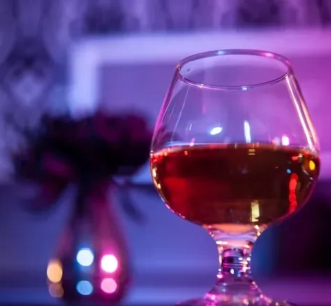 Snifter glass with amber liquid, bathed in purple and magenta light.