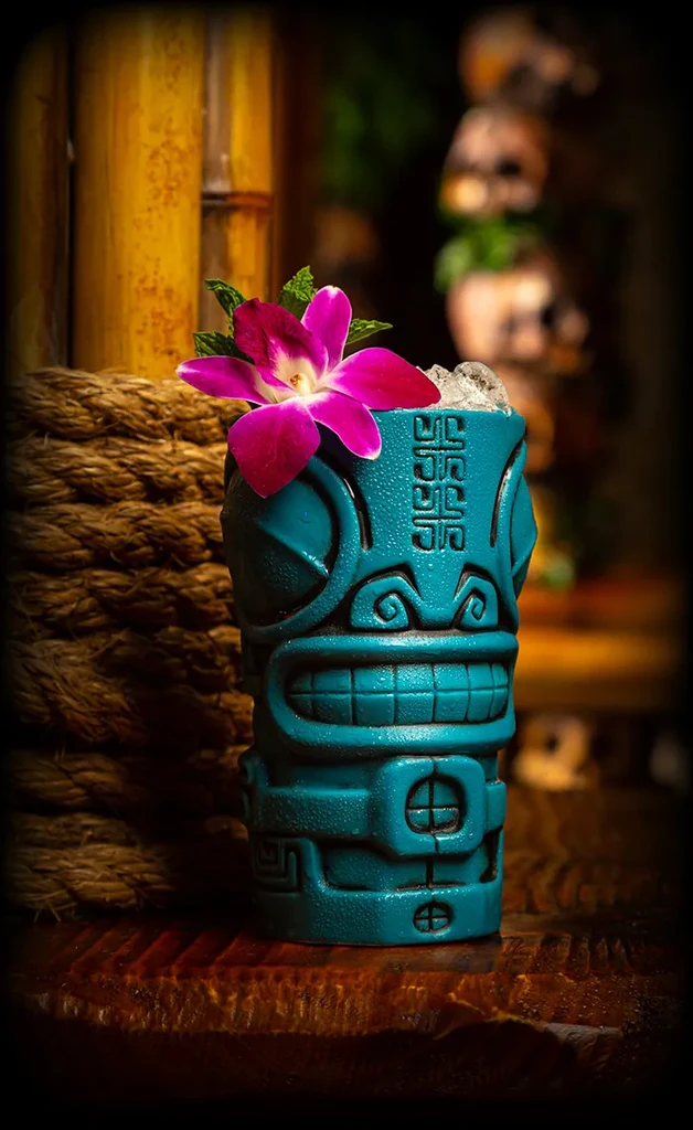 Teal tiki mug with ice, orchid, and mint on dark wood.