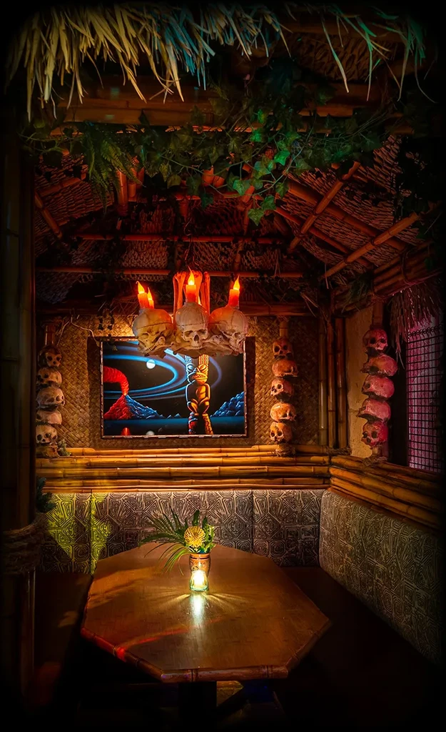 Dimly lit tiki booth with skull chandelier, volcano art, and bamboo.