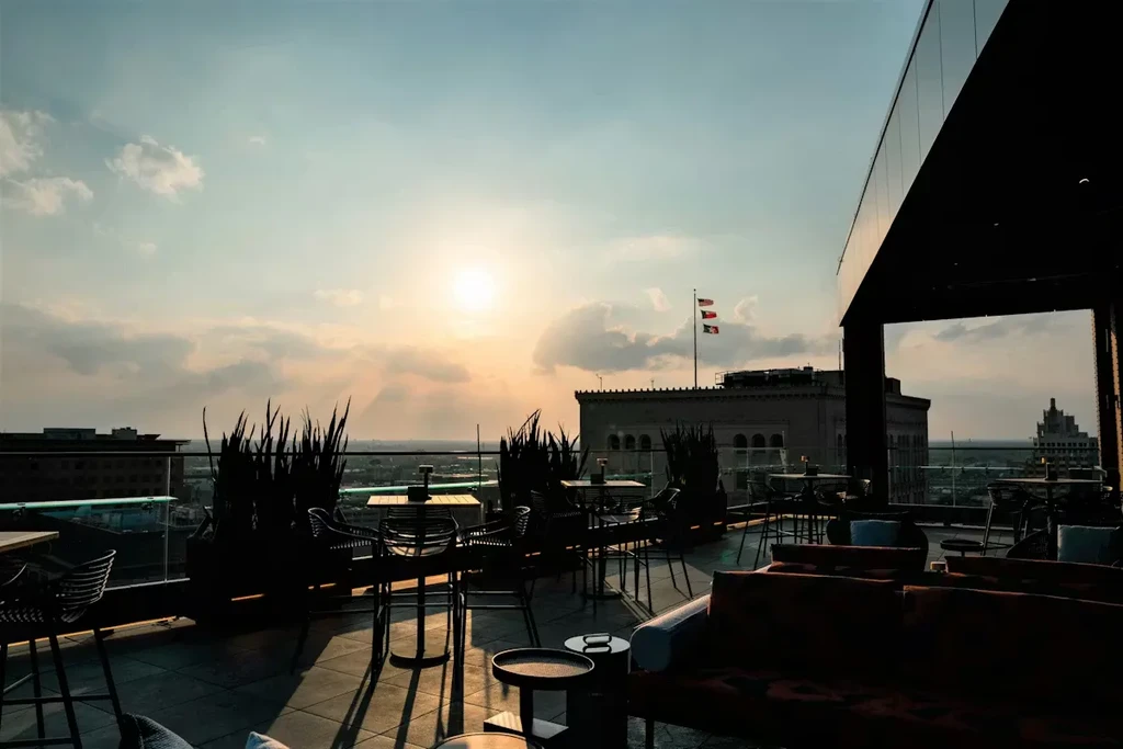 Rooftop bar terrace with silhouetted seating and sunset city view.