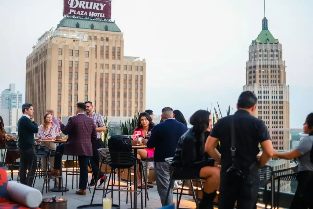 Lively rooftop bar with groups socializing, city skyline, Drury Plaza Hotel.