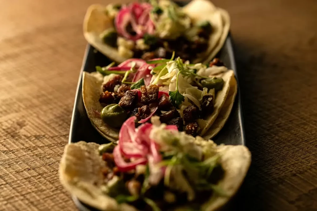 Three tacos filled with meat, green sauce, and onions on a platter.