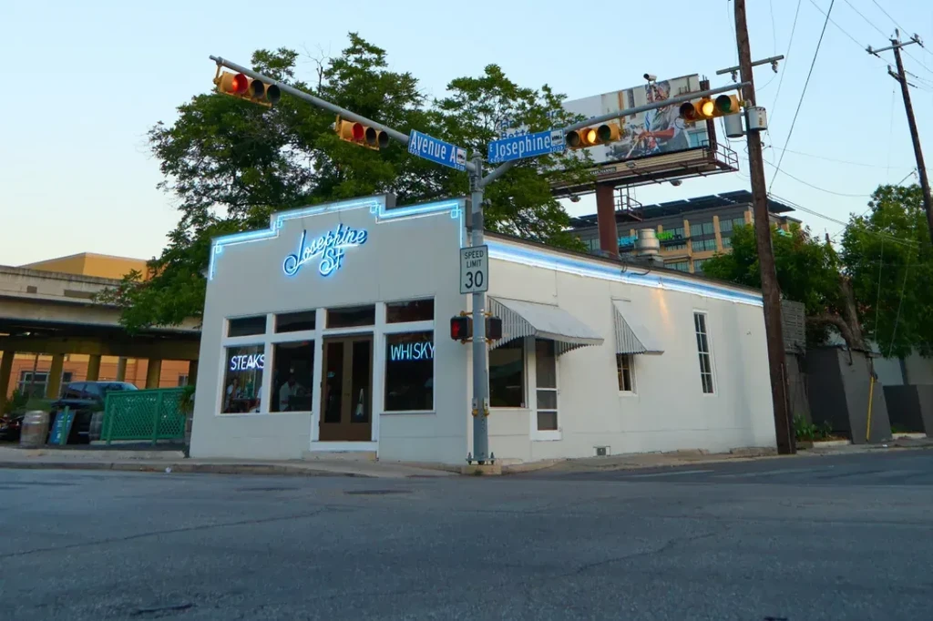 Corner building Josephine St, blue neon sign, 'STEAKS' and 'WHISKY' windows.