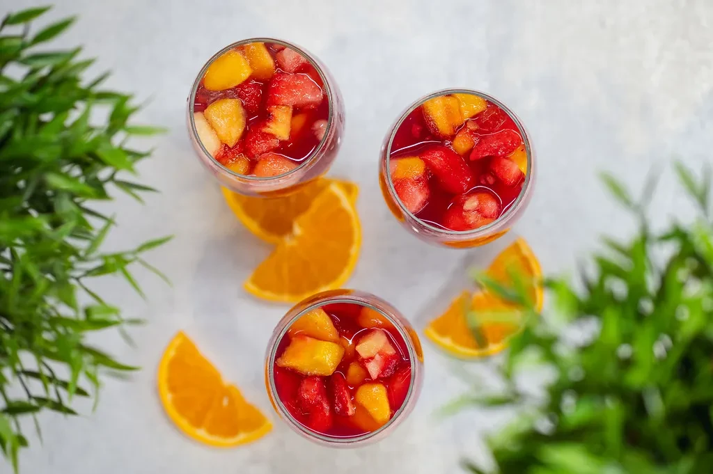 Three glasses of red fruit drink with strawberries, mango, and orange slices.