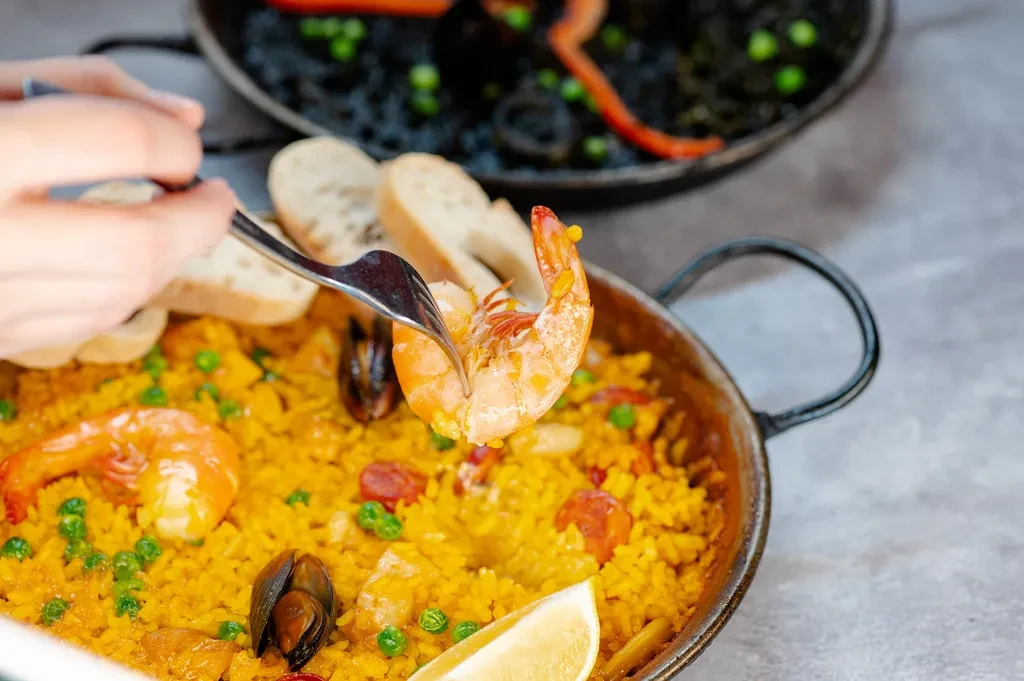 Hand forks shrimp from yellow paella with mussels and lemon.