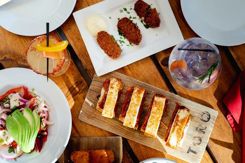 Overhead view of tapas plates and cocktails on a rustic table.
