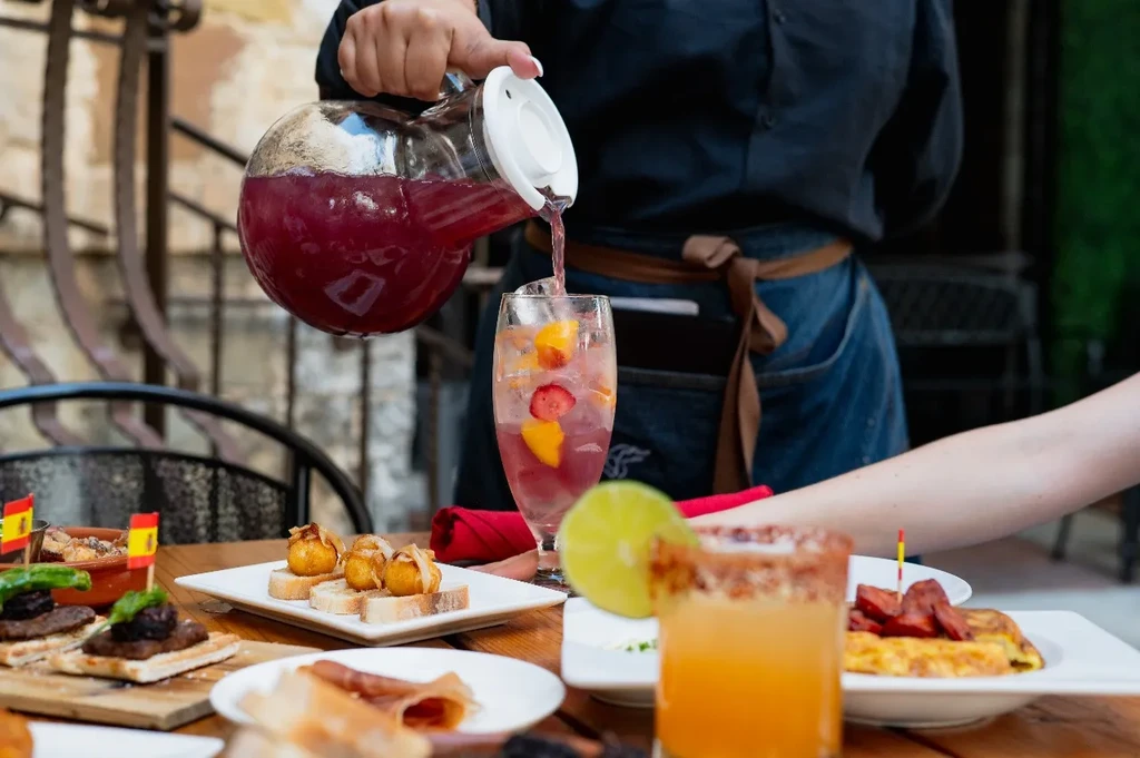 Server pours red fruit drink at an outdoor tapas restaurant.