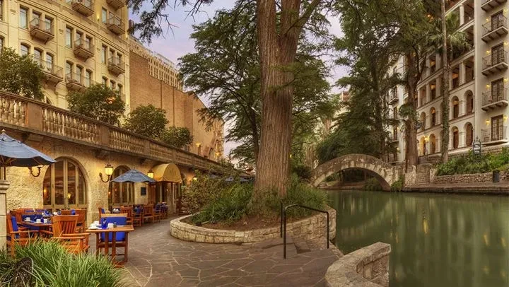 Urban riverwalk at dusk with empty dining patio and historic buildings.