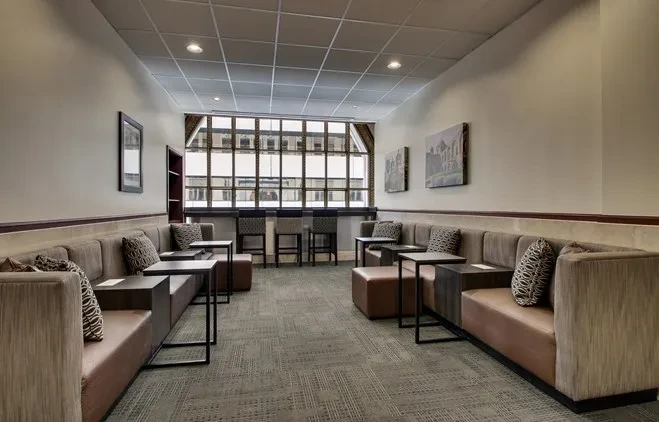 Modern, empty lounge with beige sofas, side tables, window, and framed artwork.