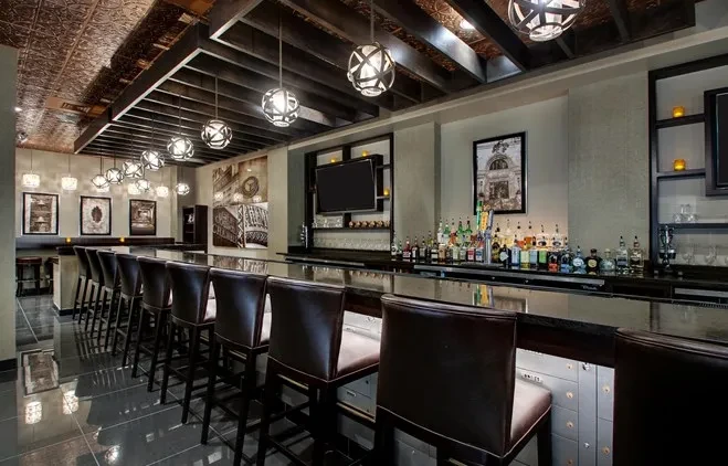 Modern bar area with dark counter, leather stools, and liquor bottles.