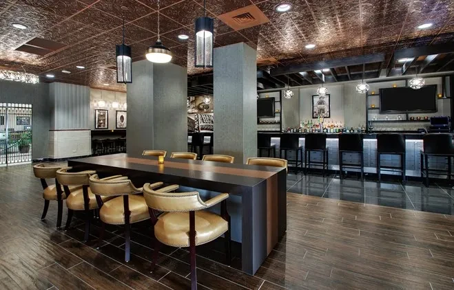 Modern restaurant interior with communal table, well-lit bar, and copper ceiling.