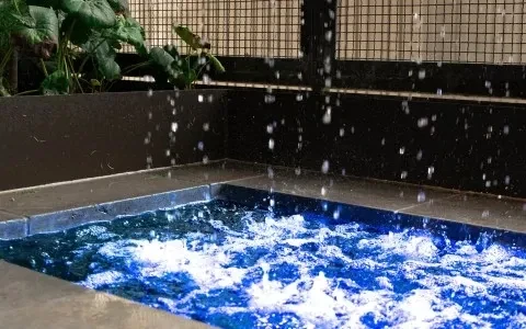Illuminated blue bubbling water feature with splashing water and green foliage.