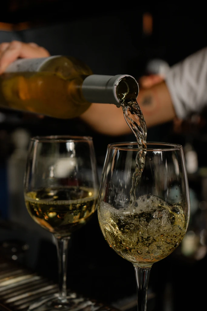 White wine pours from a bottle into a glass, splashing.