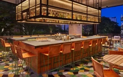 Modern outdoor bar featuring illuminated bottle shelves and vibrant geometric floor.