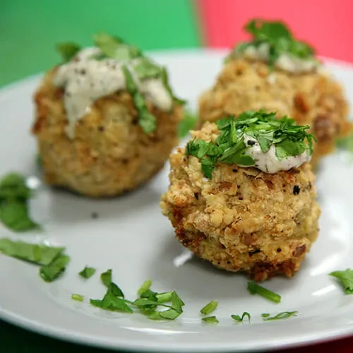 Three golden-brown fritters with sauce and herbs on a white plate.