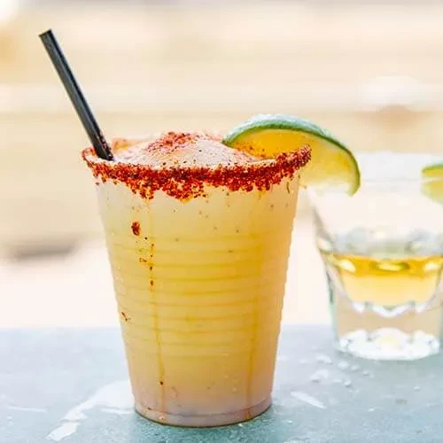 Pale yellow frozen drink with red-seasoned rim and lime wedge.