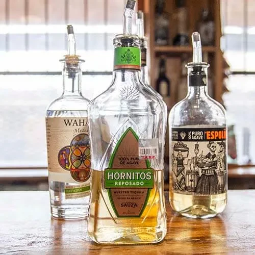 Hornitos, Wahaka, Espolon bottles with pour spouts on a wooden bar.
