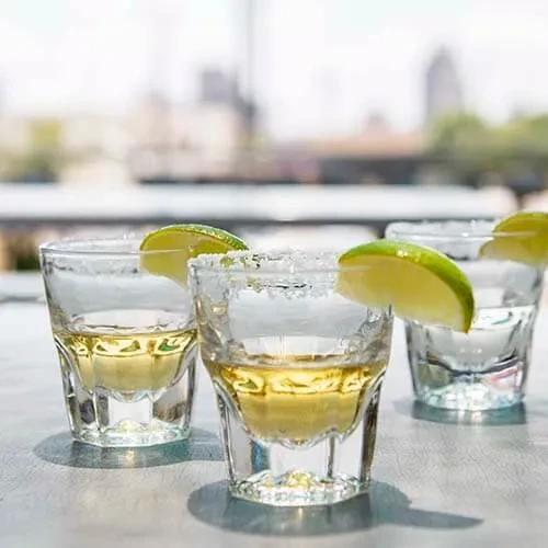 Three shot glasses with spirits, lime, and salt on a city rooftop.