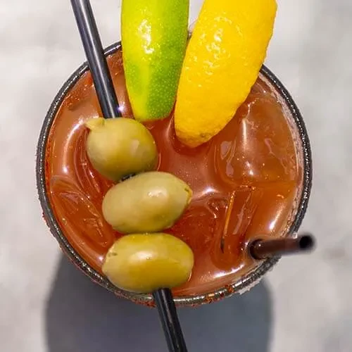 Garnished Bloody Mary cocktail with olives, lime, lemon, and straws.