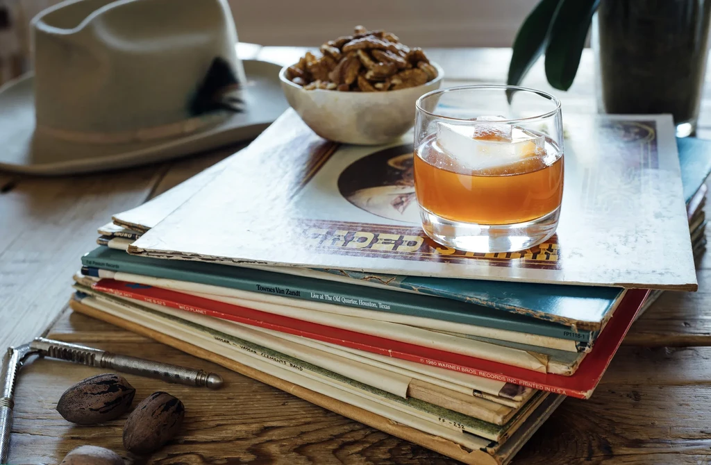 Vintage records, amber drink, pecans, and nutcracker on rustic table.