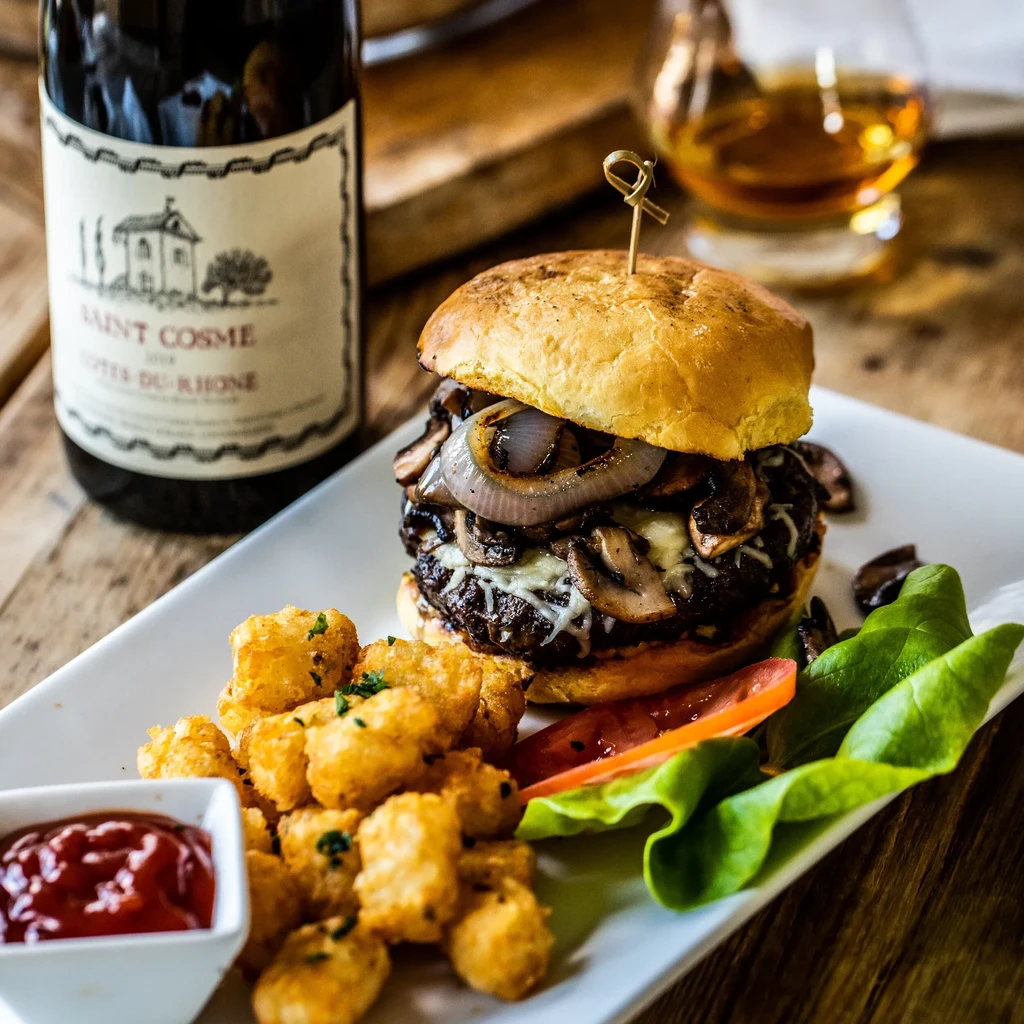 Gourmet burger with melted cheese, mushrooms, tater tots, and ketchup.