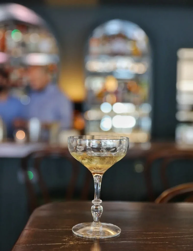 Etched coupe glass with golden drink, blurred bar interior.