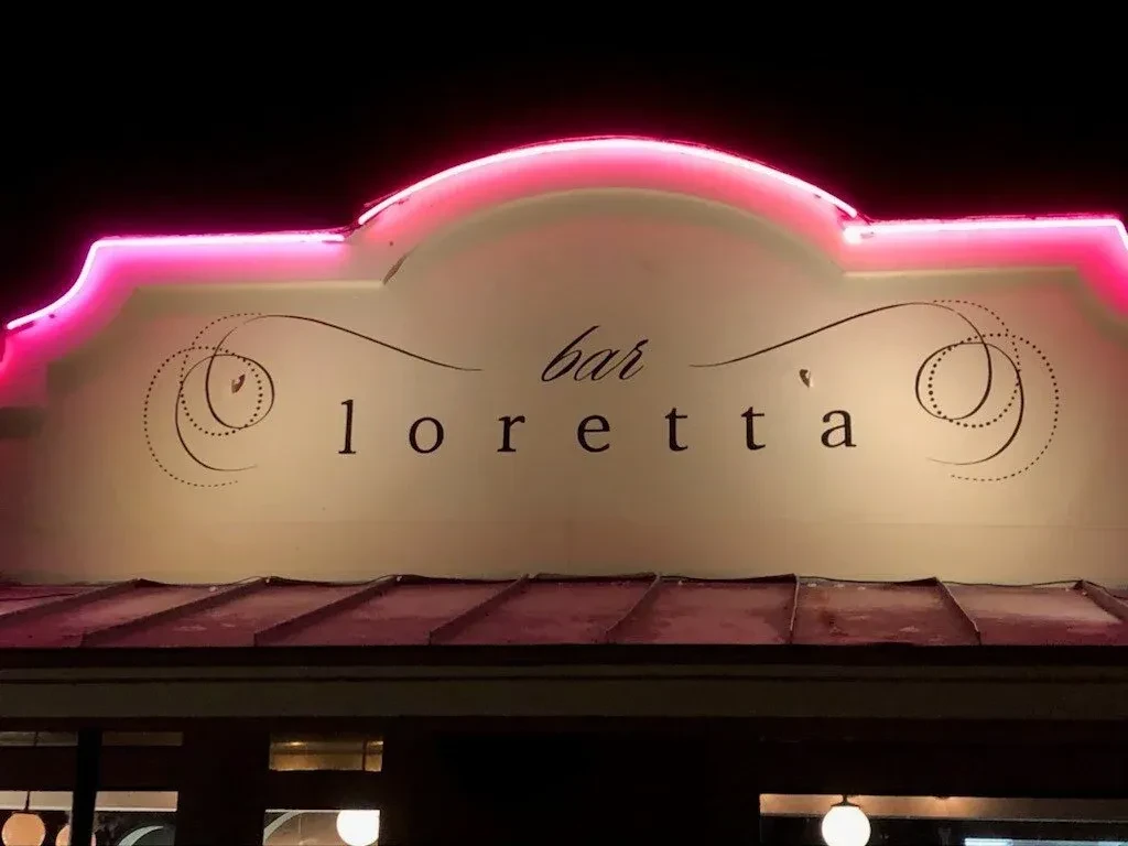 Night photo of Bar Loretta's ornate sign outlined in pink neon.
