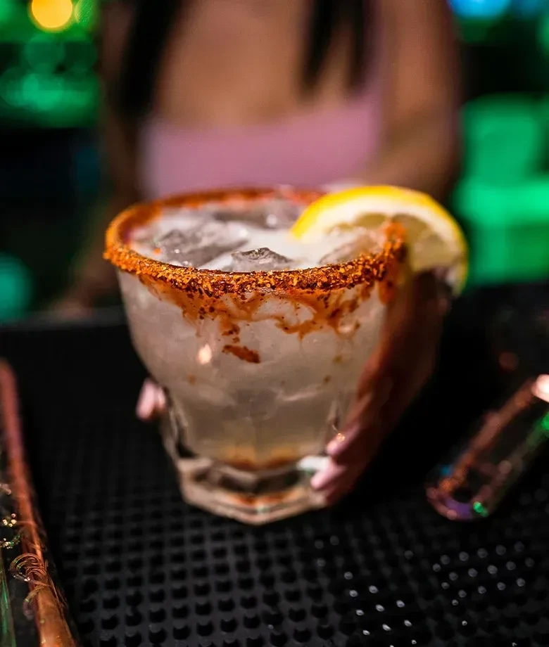 Faceted glass cocktail with chili-lime rim, lemon wedge, and ice.