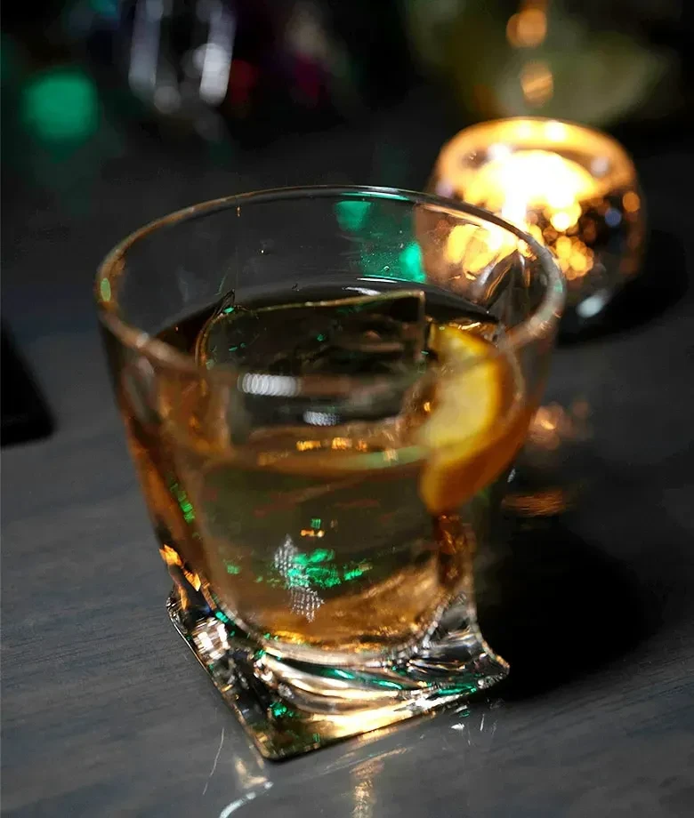 Amber drink with ice and citrus in textured glass.