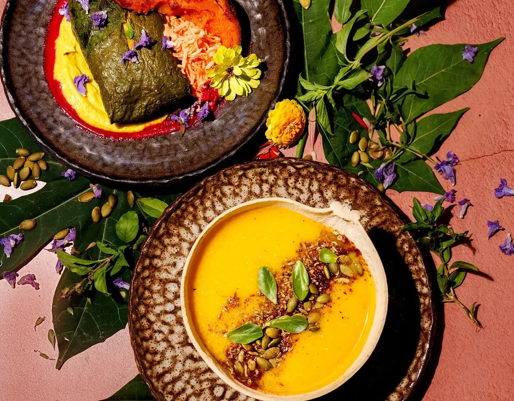 Two plated dishes, a leaf-wrapped item and yellow soup, garnished.