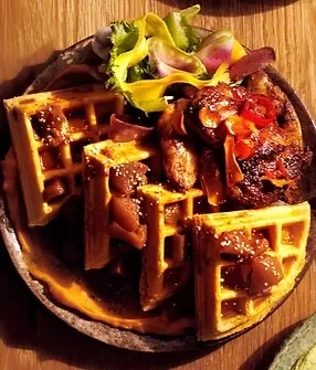 Savory waffles with fruit, meat, chili, and greens on a dark rustic plate.