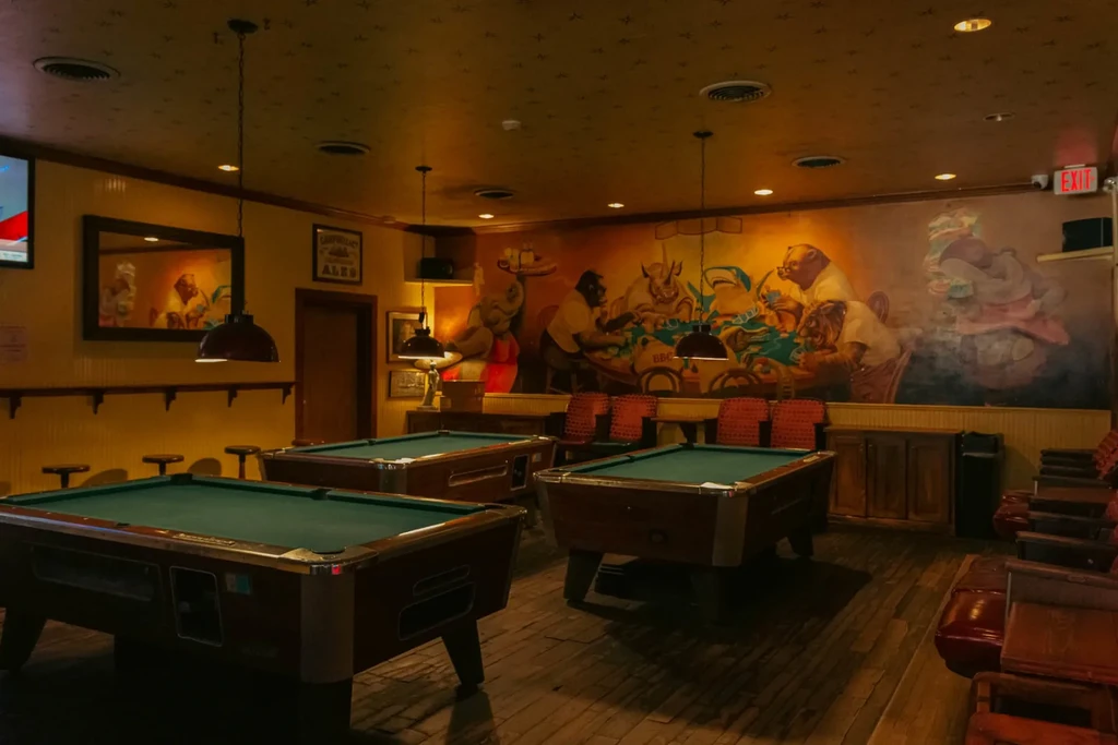 Dimly lit bar with three pool tables and an animal mural.